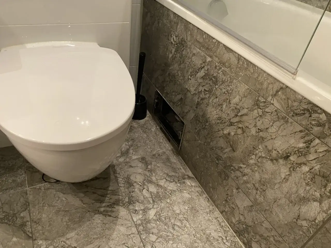 En toalett och badkar i ett modernt badrum. En toalettborste st&aring;r bredvid toaletten. Kanske en d&aring;lig lukt avlopp kan f&ouml;rklara varf&ouml;r borsten beh&ouml;vs.