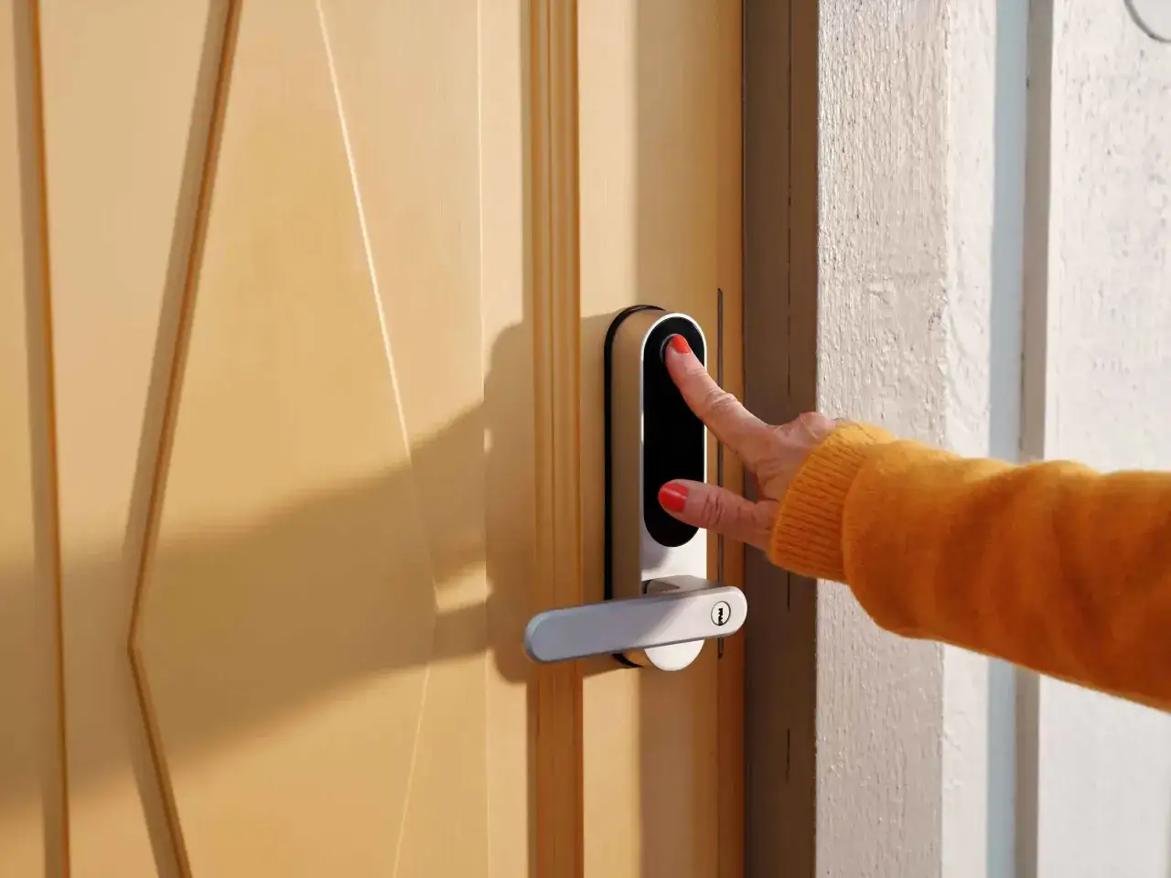 En hand med orange tröja och röda naglar testar fingeravtrycksläsaren på ett Nimly Touch Pro dörrlås.