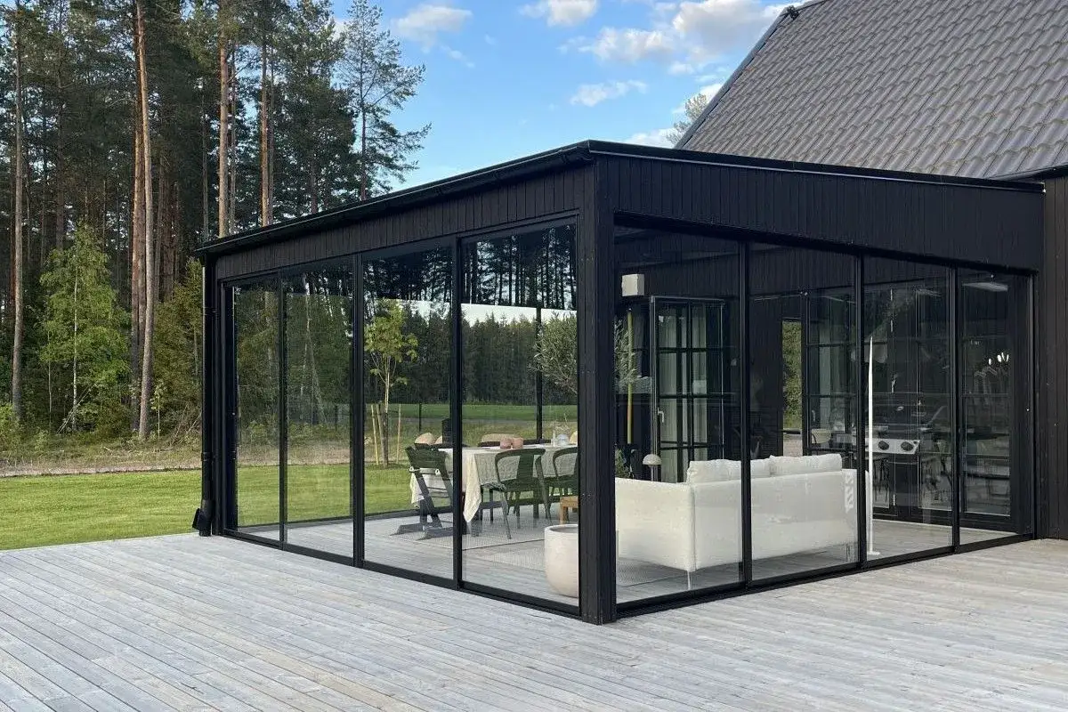 Svart modernt uterum med glaspartier som ger en k&auml;nsla av att vara utomhus, &auml;ven under vintern. H&auml;r finns soffgrupp och matplats.
