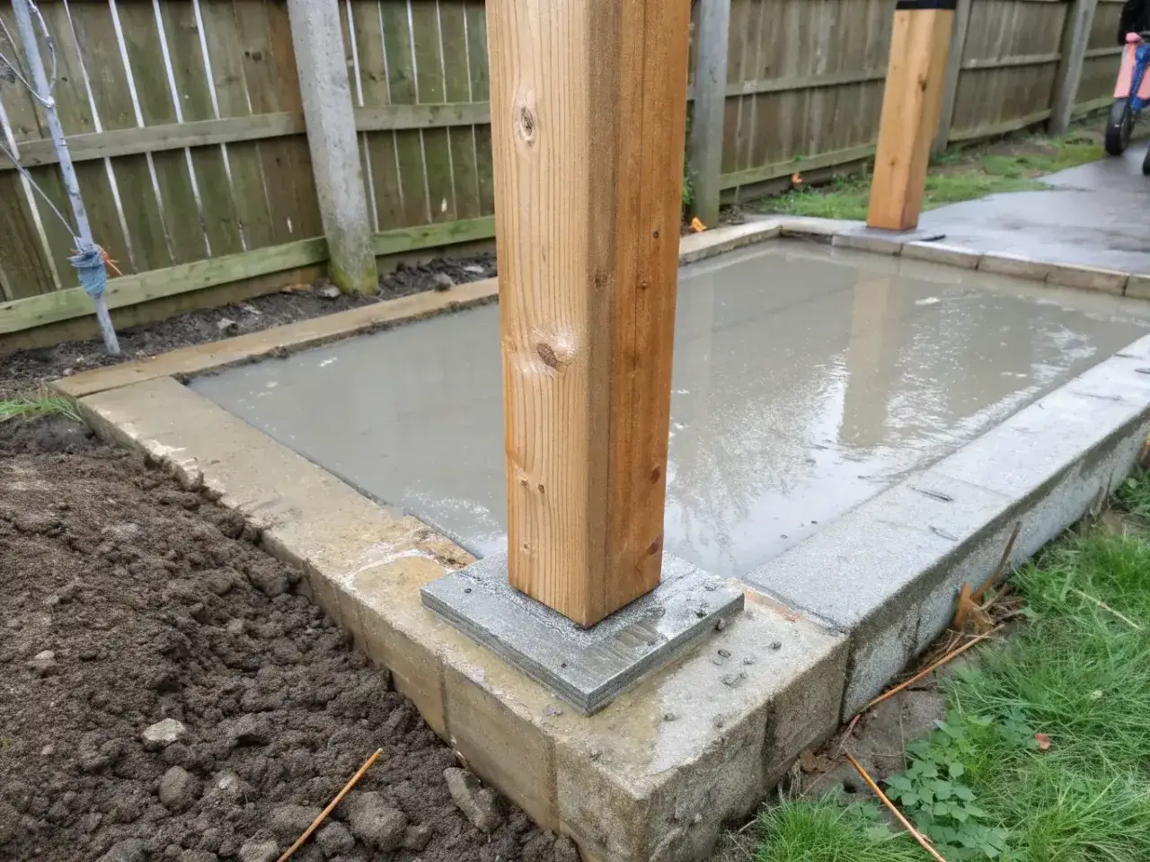Grunden för att bygga staket är på plats. En trästolpe står stadigt på en betongplatta.