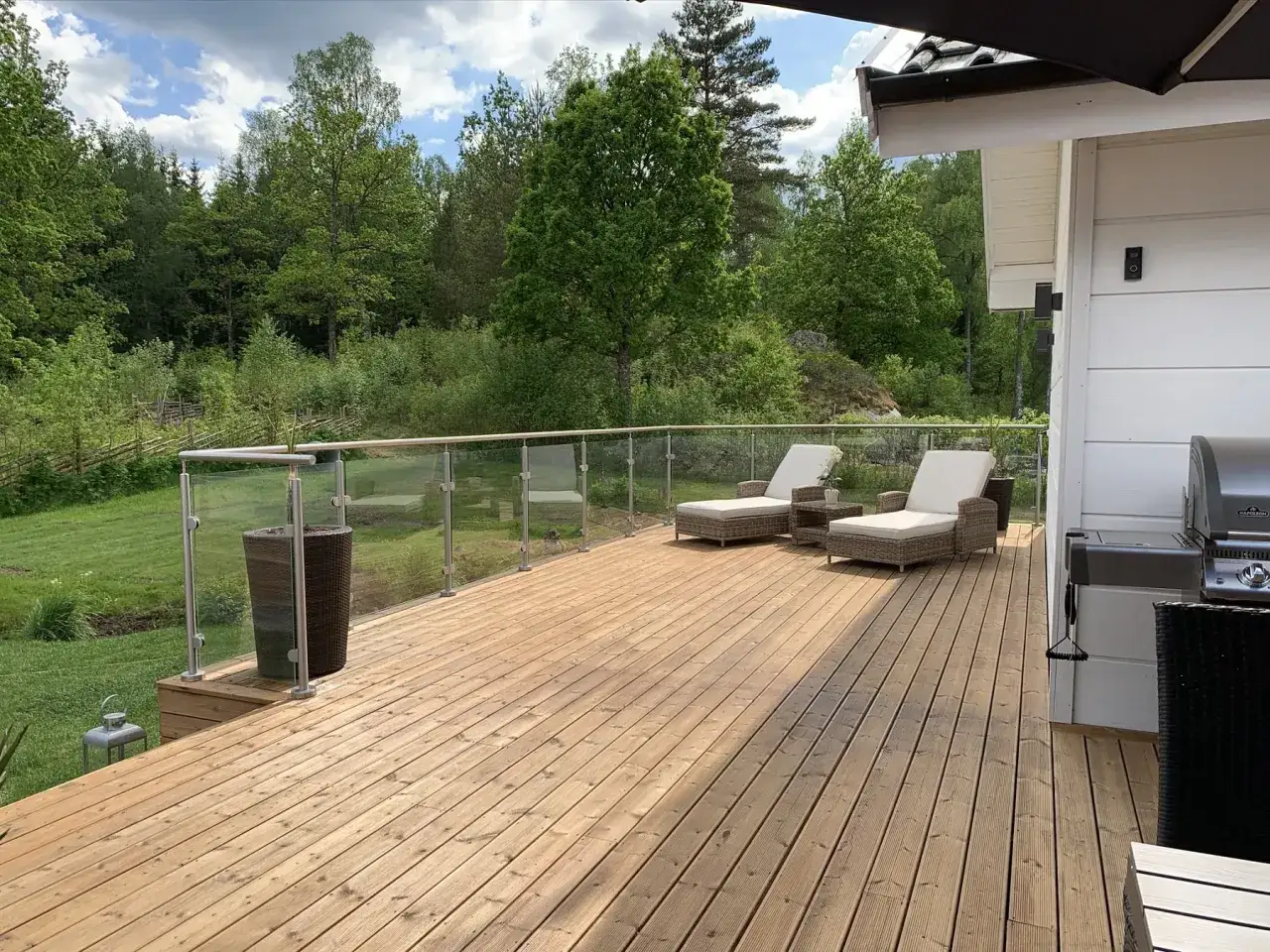 En nyoljad trall i tr&auml; med solstolar och grill. Vacker utsikt &ouml;ver skogen.